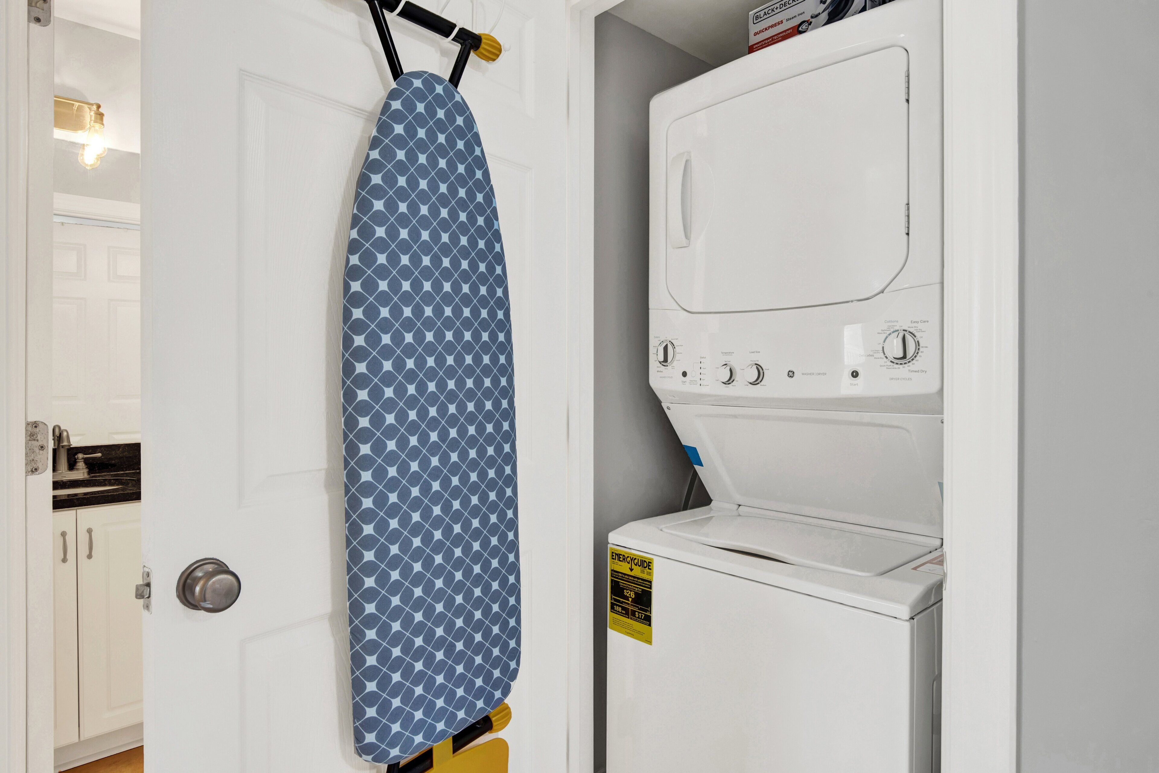 A laundry room with a white washing machine and an ironing board with a blue patterned board.