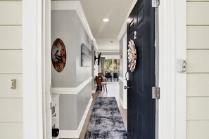 A hallway with a dark door, a wall-mounted artwork of a pelican, and a dining area with chairs and a table. - Bright Coastal Retreat on Tybee's South End | Heated Pool Access (Tybee Island)