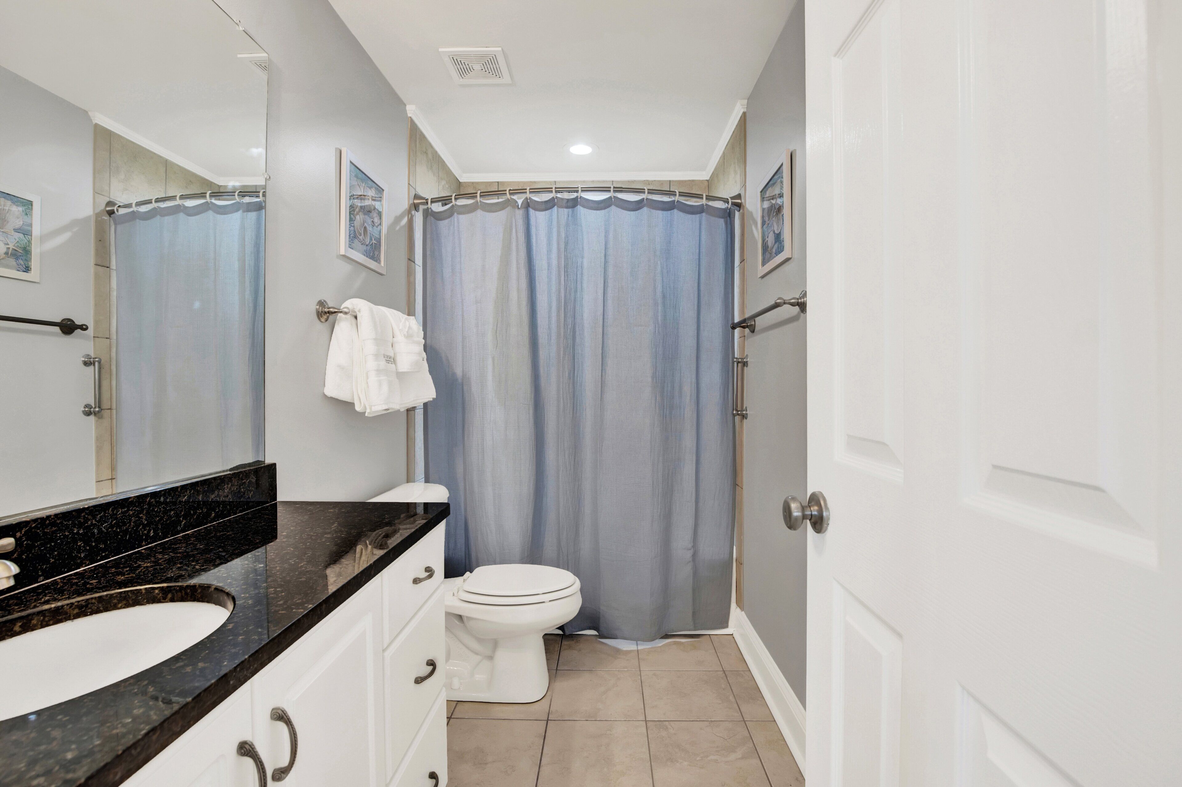 A bathroom with a white toilet, a black marble sink, and a shower curtain.