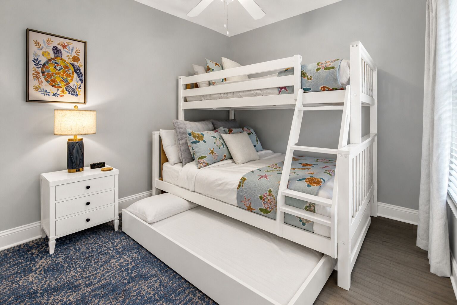 A bunk bed with a nightstand and drawers, a framed picture on the wall, and a ceiling fan.