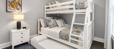 A bunk bed with a nightstand and drawers, a framed picture on the wall, and a ceiling fan.