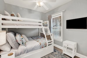A child's bunk bed with a TV on the wall, a small table, and a window with blinds. - Bright Coastal Retreat on Tybee's South End | Heated Pool Access (Tybee Island)