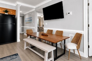 A modern kitchen with a black refrigerator, a wooden dining table with benches, and wicker chairs. - Bright Coastal Retreat on Tybee's South End | Heated Pool Access (Tybee Island)