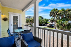 A balcony with a table and chairs, a door, and a view of palm trees and a street. - Bright Coastal Retreat on Tybee's South End | Heated Pool Access (Tybee Island)