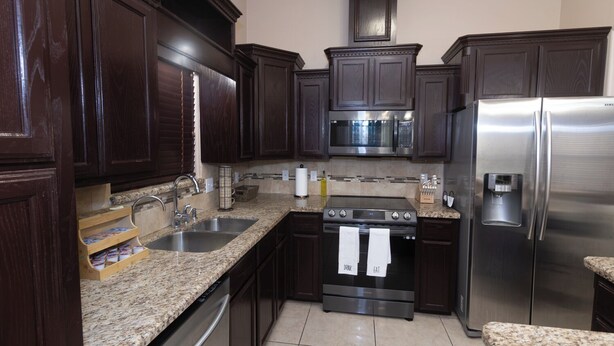 A kitchen with dark wood cabinets, stainless steel appliances, granite countertops, and a built-in oven.