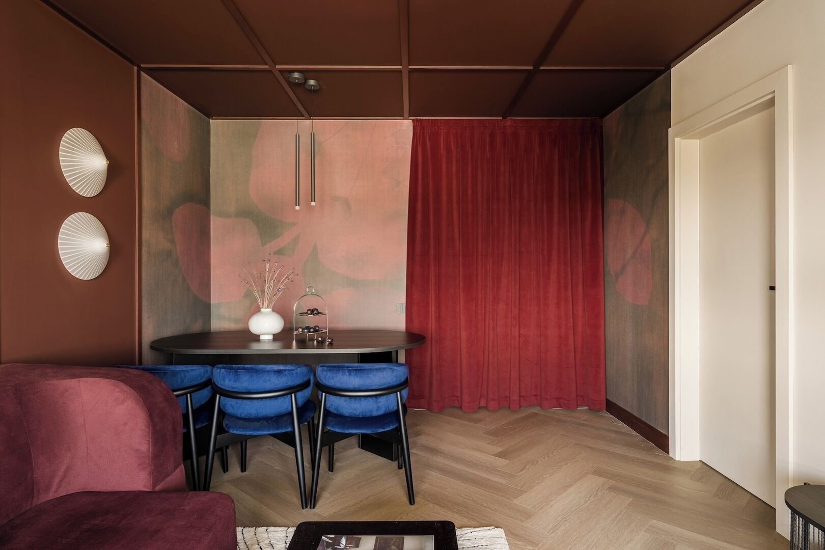 Un espace repas moderne avec une table ronde, des chaises bleues et un rideau rouge.