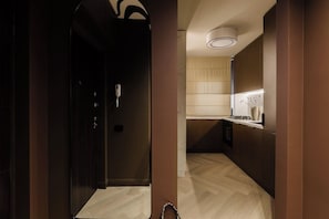 A modern interior with a wooden floor, a kitchen area with a countertop and a hanging light fixture, and a dark-toned door. - Velvet Noir Old Town (Bucharest)