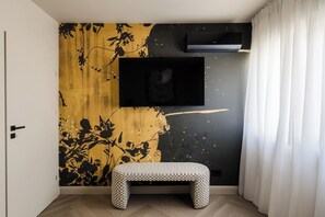 Um quarto com um banco, uma TV fixada na parede e um papel de parede floral.