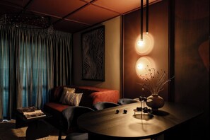 A modern living room with a sofa, a coffee table, and a dining table. There are two pendant lights hanging from the ceiling. - Velvet Noir Old Town (Bucharest)