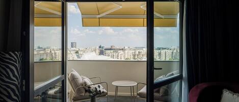 A balcony with a city view, a cushioned chair, a small table, and a red armchair.