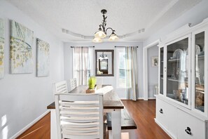 A dining area with a wooden table, white chairs, a chandelier, and a cabinet with glass doors. - Hudson House | 0.2 Miles to Red River (1726 Broadripple Drive) (Clarksville)