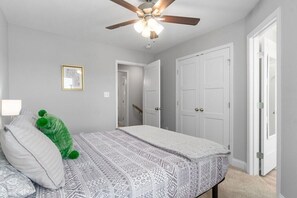 Une chambre à coucher avec un lit, un ventilateur de plafond et une porte donnant sur une autre pièce.