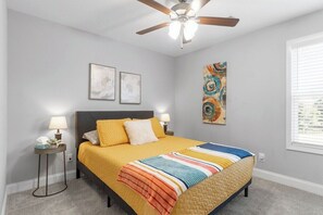 Ein Schlafzimmer mit einem Bett, zwei Nachttischen, einem Deckenventilator und Kunstwerken an den Wänden.