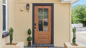 En beige byggnad med en brun dörr, nummer 5, och två små krukväxter på var sin sida.