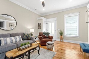 A living room with a sofa, armchair, coffee table, and ottoman. There is a large mirror, a lamp, and a potted plant. - Todd's Place in Downtown (638 Madison St, #5) (Clarksville)