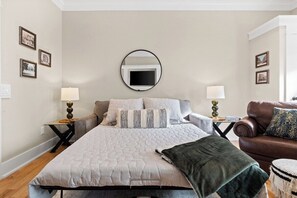 A bedroom with a large bed, two bedside tables with lamps, a brown leather sofa, and a round mirror on the wall. - Todd's Place in Downtown (638 Madison St, #5) (Clarksville)