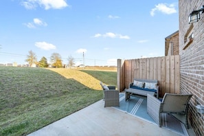 Ein Patio mit Holzzaun, Backsteinmauer und Gartenmöbeln.