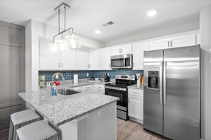 Eine moderne Küche mit weißen Schränken, Edelstahlgeräten, Granit Arbeitsplatten und Barhocker.