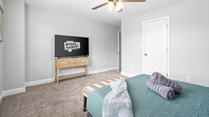Un dormitorio con una cama, un ventilador de techo, un televisor sobre un soporte de madera y una puerta.