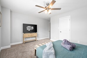 Ein Schlafzimmer mit Bett, Deckenventilator, Fernseher auf einem Holzboden und einer Tür.