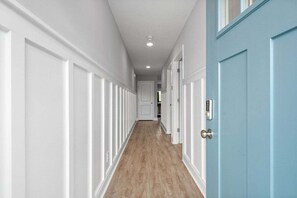 Un pasillo con paneles de madera blanca, una puerta azul y suelo de madera.