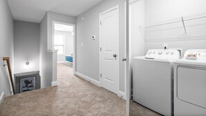 Un lavadero con dos lavadoras y secadoras blancas, una puerta blanca y un pasillo que lleva a una habitación con ventanal.