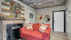 Una habitación con chimenea, un sofá rojo, una obra de arte de madera en la pared y una puerta.