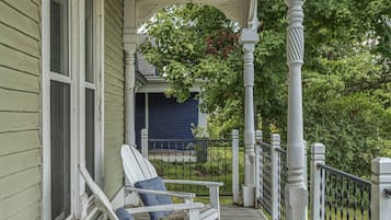 A porch with two white Adirondack chairs, a wooden deck, and a white railing.
