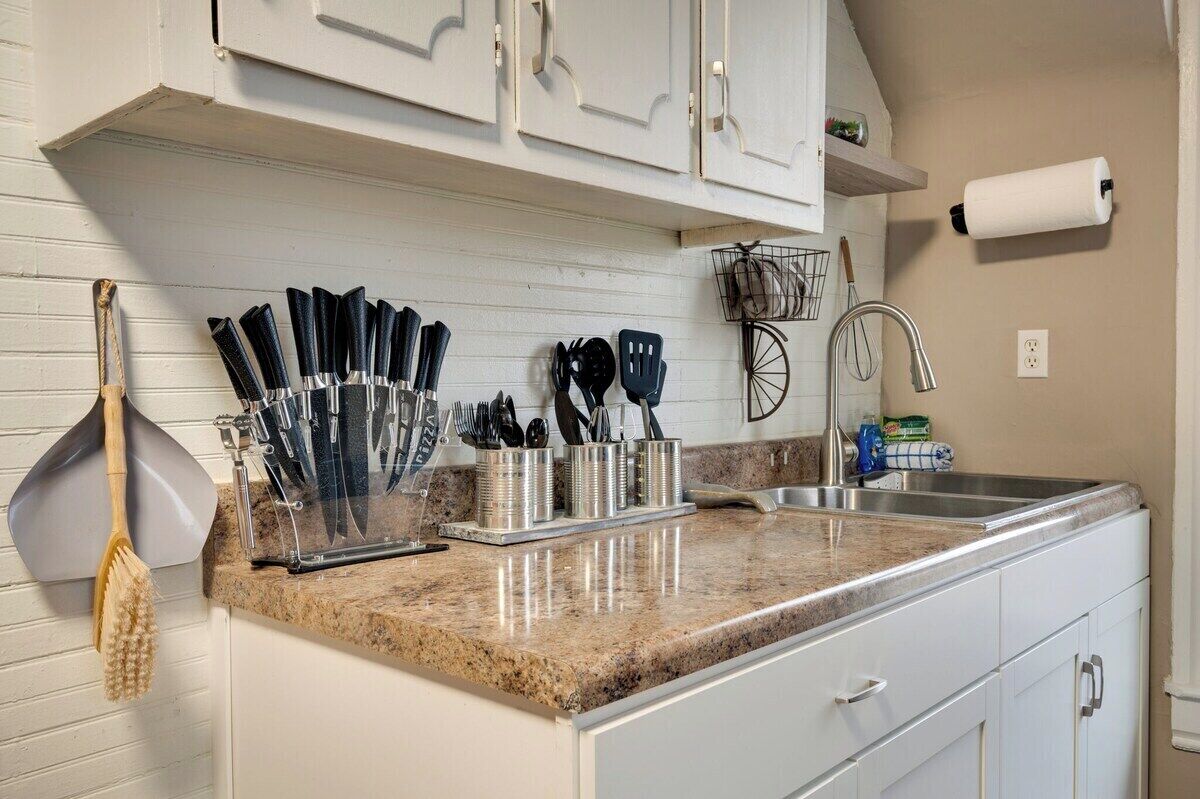 A kitchen with white cabinets, a granite countertop, and various utensils.
