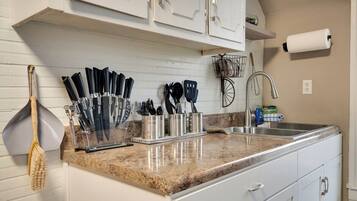 A kitchen with white cabinets, a granite countertop, and various utensils.