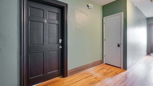 Un pasillo con una puerta negra marcada con el número 4, una puerta blanca y suelo de madera.