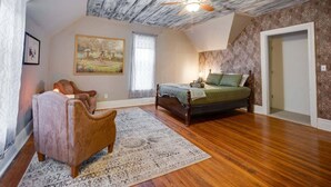 Un dormitorio con techo de madera, una cama con manta verde, un sillón antiguo y un cuadro grande en la pared.