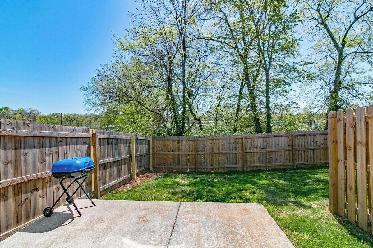 Ein Garten mit einer Beton-Terrasse, einem Holzzaun und einem blauen Grill.