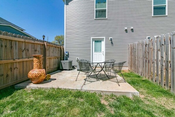 A backyard with a concrete patio, a metal table and chairs, a large decorative vase, and a wooden fence.