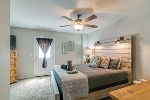 A bedroom with a bed, a ceiling fan, a window with curtains, a wooden dresser, and a bedside table.