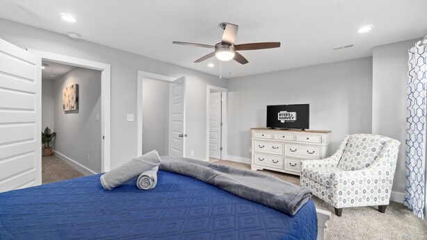Ein Schlafzimmer mit Bett, Deckenventilator, Kommode, Stuhl und Fernseher.