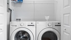 Ein Waschbereich mit zwei weißen LG Waschmaschinen mit Frontlader, einem Metallregal mit Waschmitteln und einer weißen Tür.