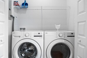 A laundry area with two white LG front-loading washing machines, a metal shelf with laundry supplies, and a white door. - Rebecca's Downtown Luxury Living (527 N 1st St) (Clarksville)