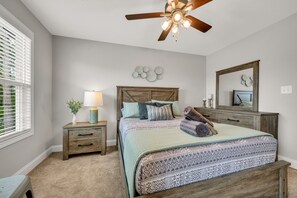 Un dormitorio con cama, mesitas de noche, ventilador de techo, cómoda, espejo y decoración en las paredes.