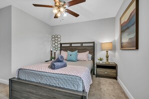 Ein Schlafzimmer mit einem Bett, einem Nachttisch, einer Lampe, einem Deckenventilator und einem Wandbild.