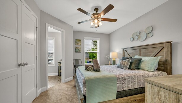 A bedroom with a bed, a ceiling fan, a nightstand, a lamp, and a view of the outdoors through a window. - Tee Time Treasures in Sango (1625 Golf Club Ln, #602) (Clarksville)