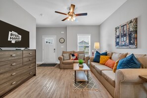 Ein modernes Wohnzimmer mit Flachbildfernseher, Deckenventilator, Sofa, Couchtisch und einem Gemälde an der Wand.
