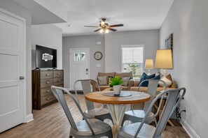 Ein modernes Wohnzimmer mit Deckenventilator, Fernseher, Sofa und Esstisch mit Stühlen.