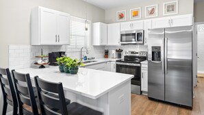 Una cocina moderna con armarios blancos, electrodomésticos de acero inoxidable, una isla central con sillas y una cafetera.