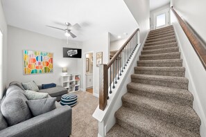 A living room with a gray couch, a colorful abstract painting, a television, and a staircase with a wooden railing. - Adam's Downtown Retreat with 2 Rooftop Patios (Clarksville)