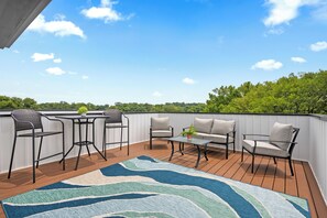 A deck with outdoor furniture, including chairs and a table, and a view of the sky and trees. - Adam's Downtown Retreat with 2 Rooftop Patios (Clarksville)