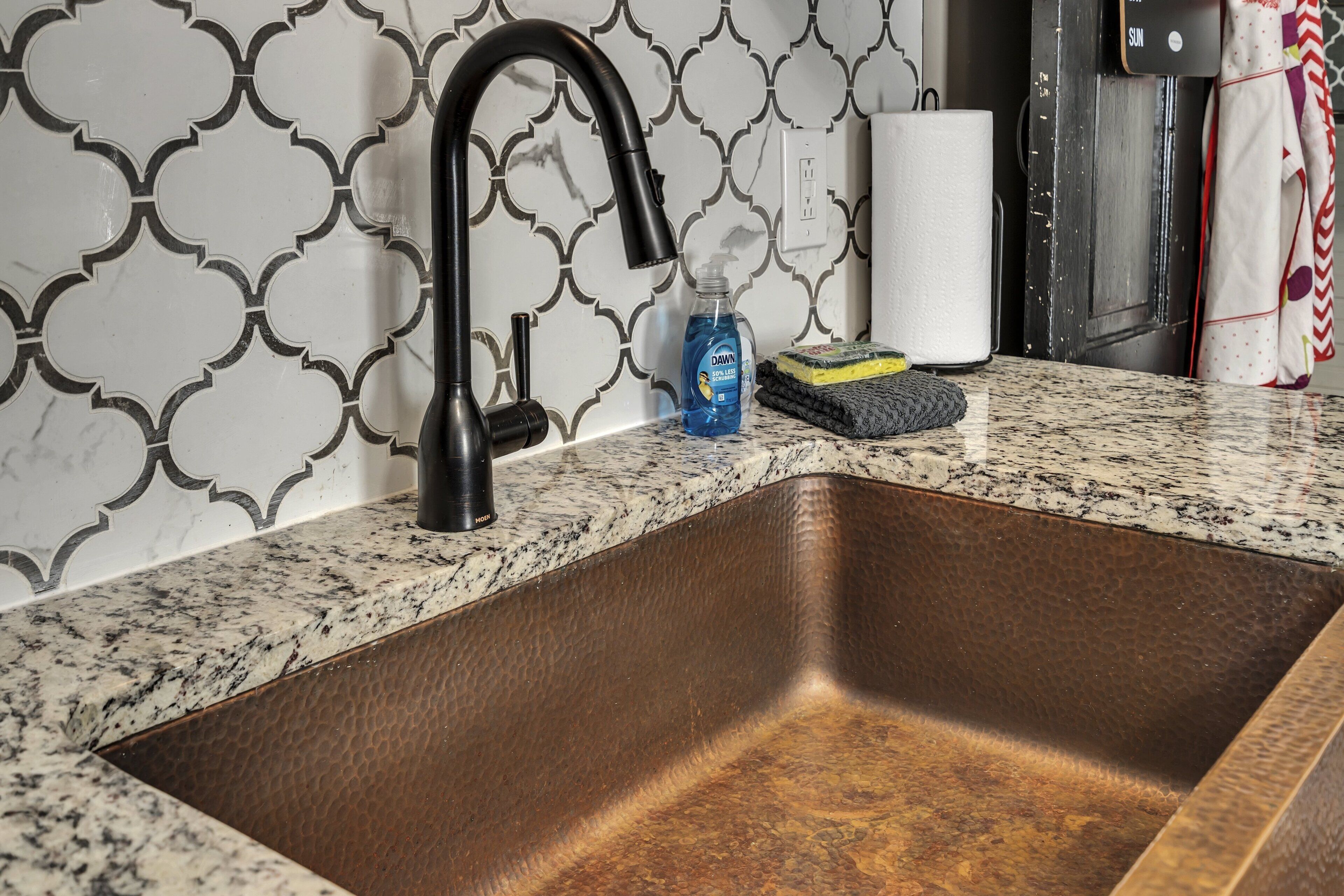 A kitchen with a stainless steel sink, a black faucet, and a patterned backsplash.