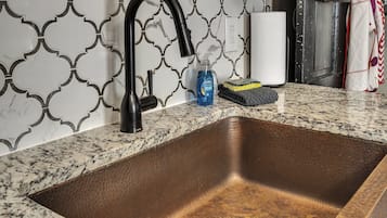 A kitchen with a stainless steel sink, a black faucet, and a patterned backsplash.
