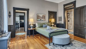 Quarto com cama, luminárias de cabeceira, um quadro, uma porta e vista para a cozinha.