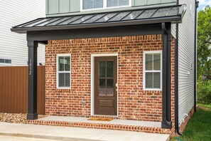Une maison à deux étages avec une façade en briques, une porte d’entrée dotée d’une fenêtre et un petit porche.